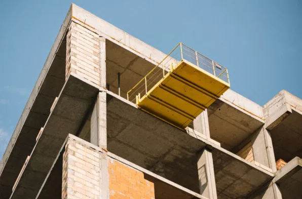 Unfinished building with exposed brick and concrete framework; a yellow construction platform extends from the upper floor.